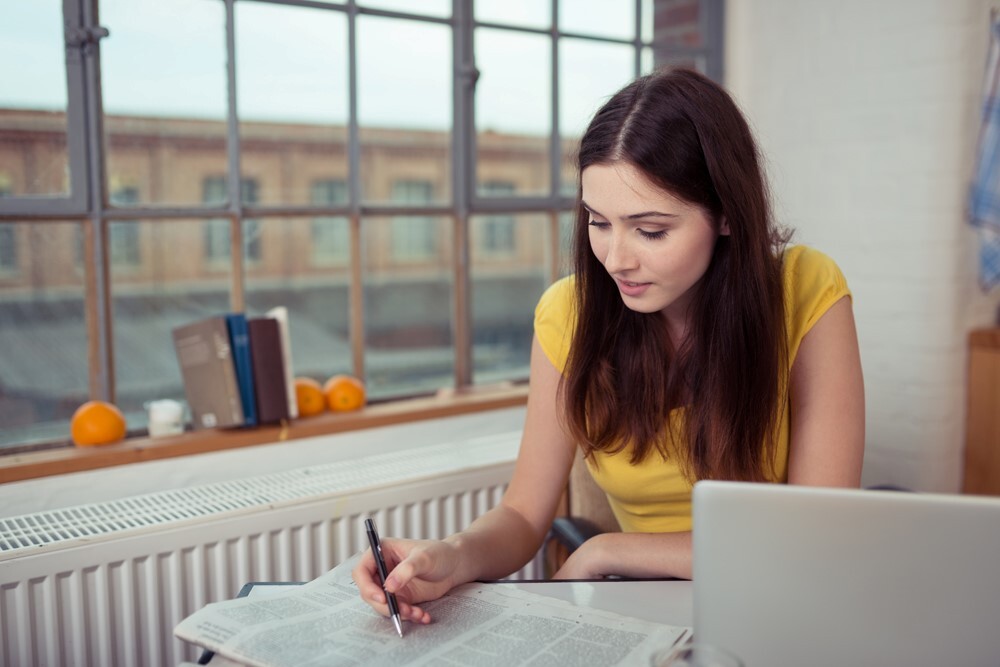 woman looking at newspaper and marking it with a pen