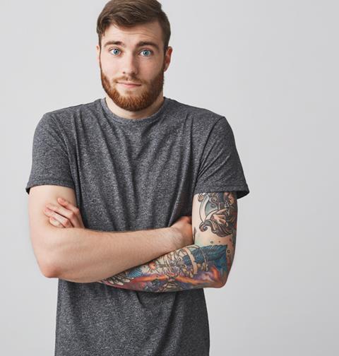 young guy wearing t-shirt that reveals arm tattoo, looking puzzled