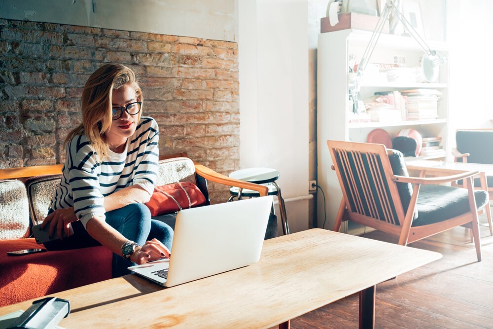 woman on couch working on laptop that sits on coffee table